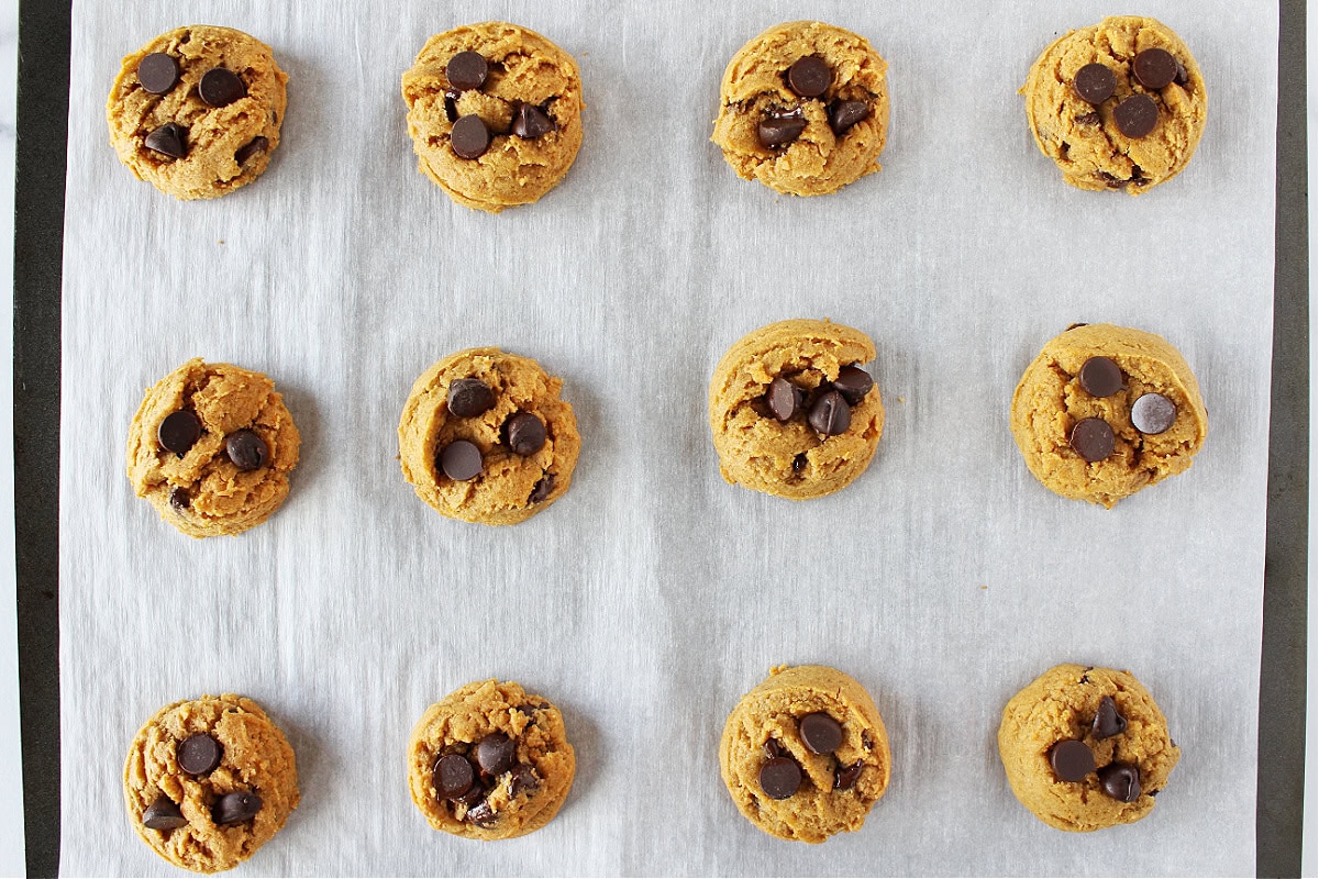 Chocolate chips pressed into the tops of twelve freshly baked cookies.