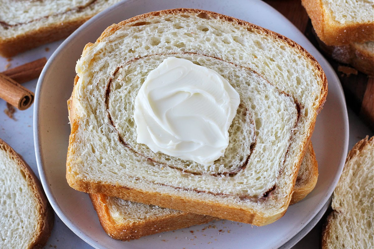 Softened butter on two cinnamon swirl sourdough bread slices on a white plate.