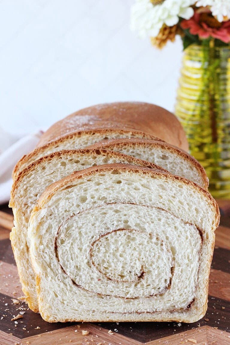 Cinnamon swirl sourdough bread slices next to loaf on a wooden cutting board.