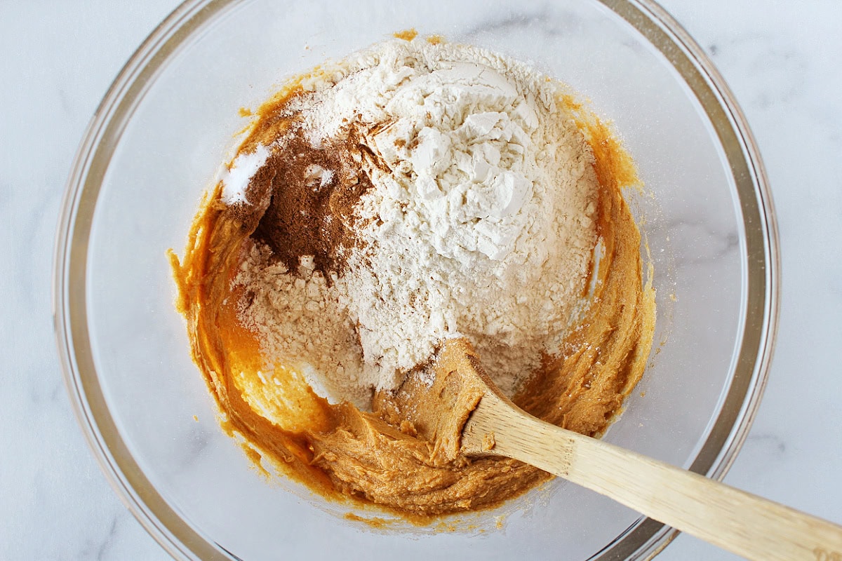 Flour and dry ingredients on top of wet batter in a glass bowl.