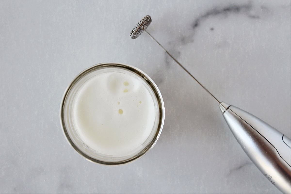 Frothed half and half in a glass mug with a handheld frother.