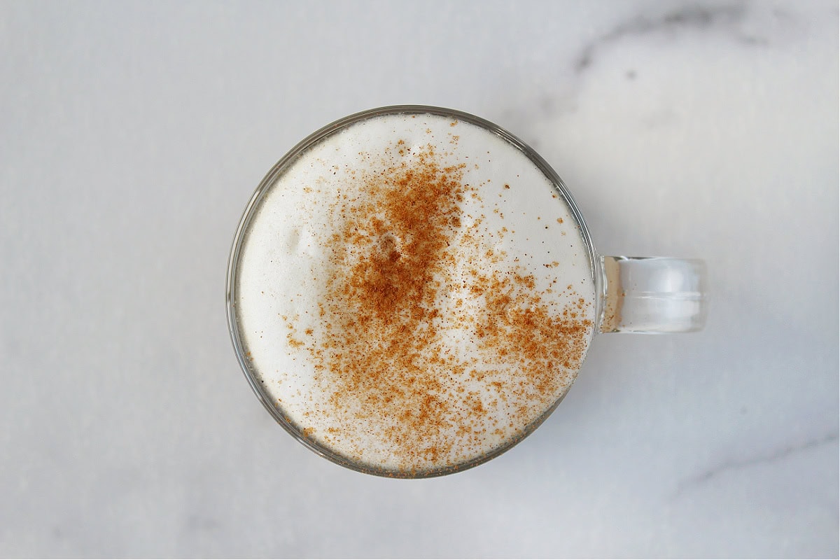 Frothed half and half in a glass mug topped with pumpkin pie spice.
