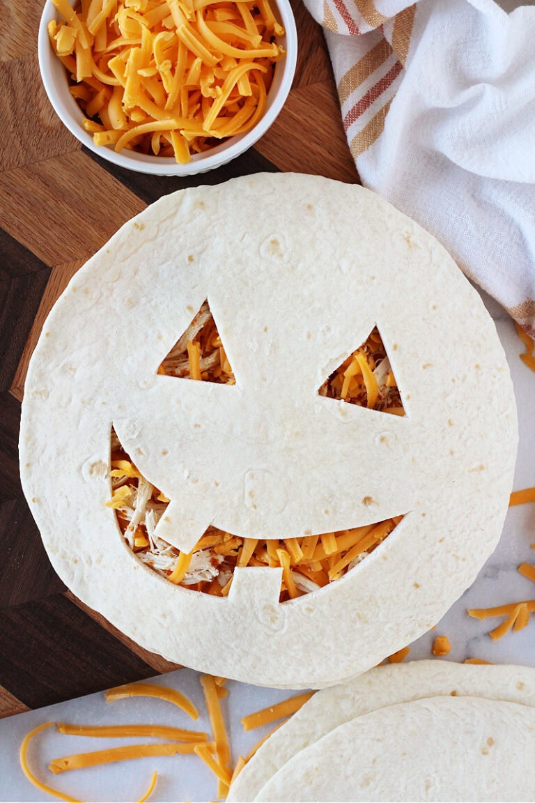 An uncooked chicken and cheese Jack O' lantern quesadilla on a cutting board.