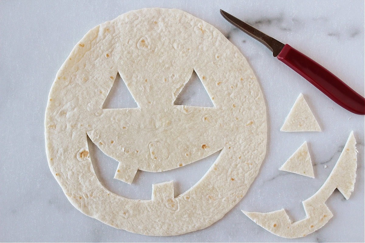 A knife cut a jack o' lantern face out of a flour quesadilla.