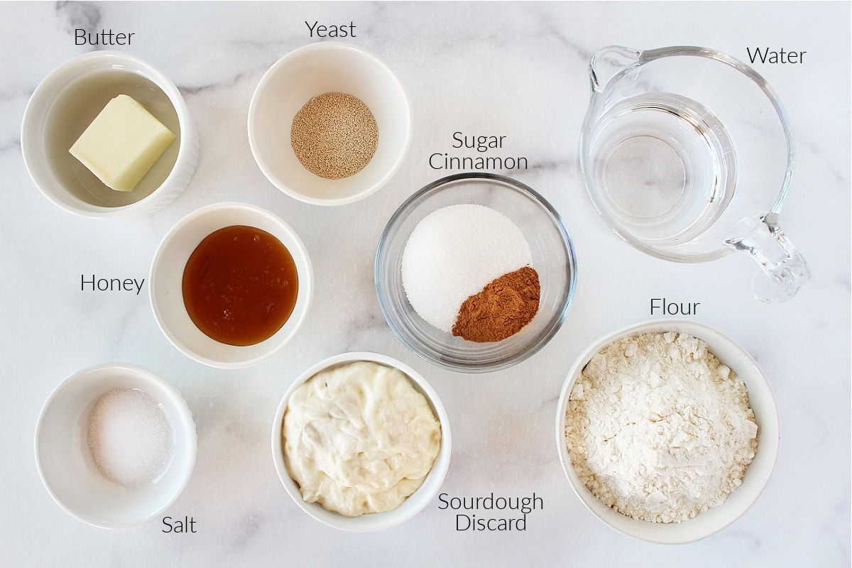 Labeled ingredients for cinnamon sourdough sandwich bread on a white marble countertop.