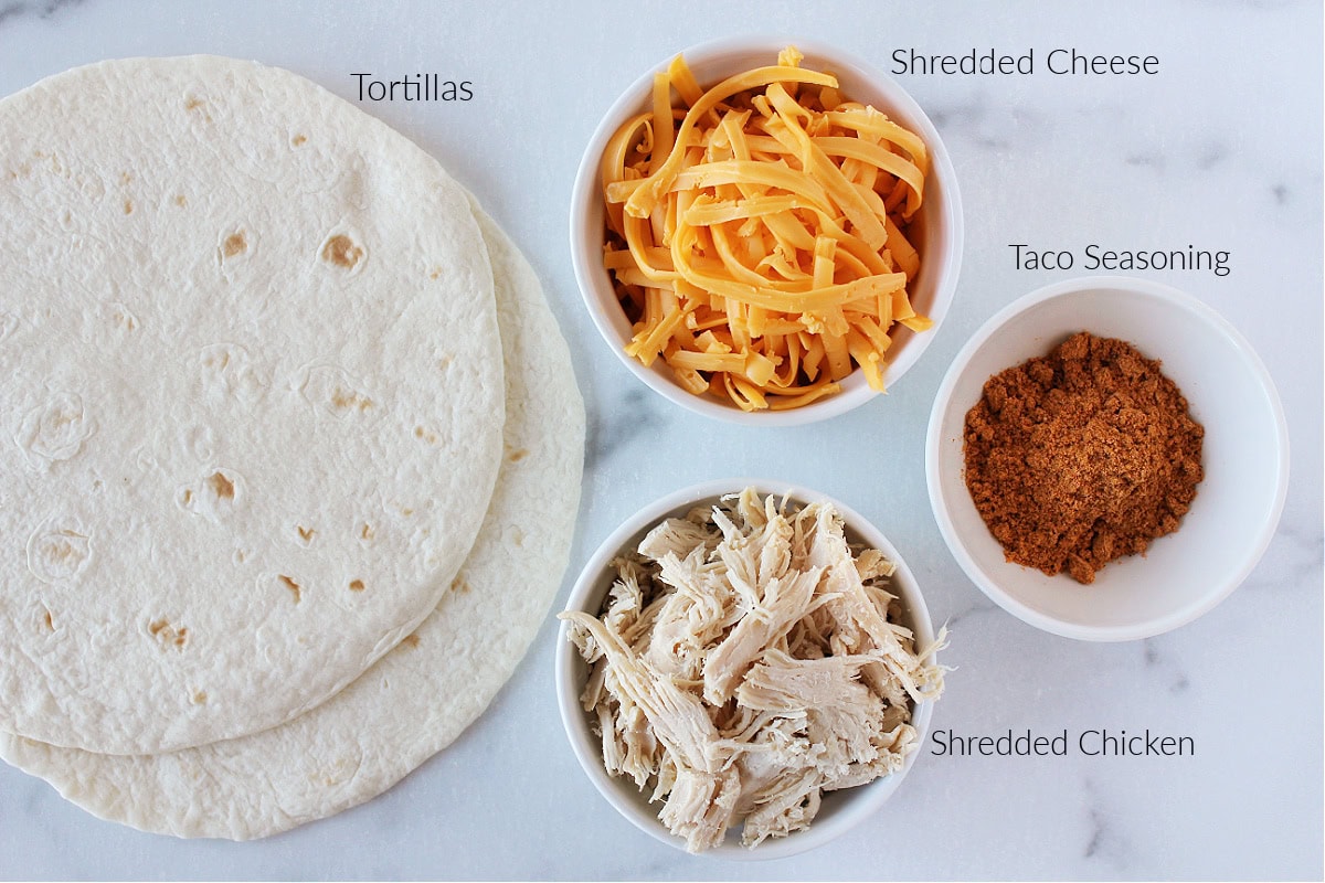 Labeled ingredients for jack o' lantern quesadillas with shredded chicken on a white marble countertop.