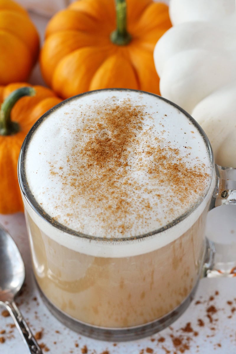 A homemade pumpkin spice latte in a mug with orange and white pumpkins.