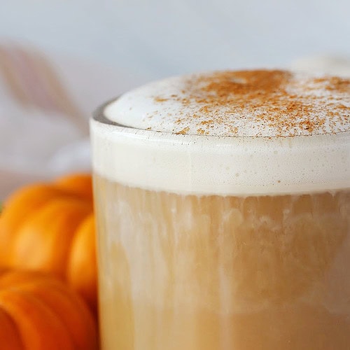 Tiny orange pumpkins beside a mug of homemade pumpkin spice latte.