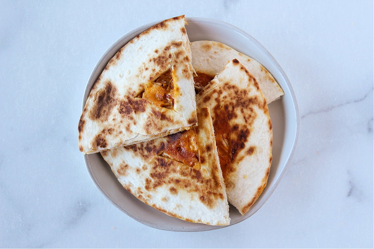 A quesadilla cut into four pieces on a white plate.