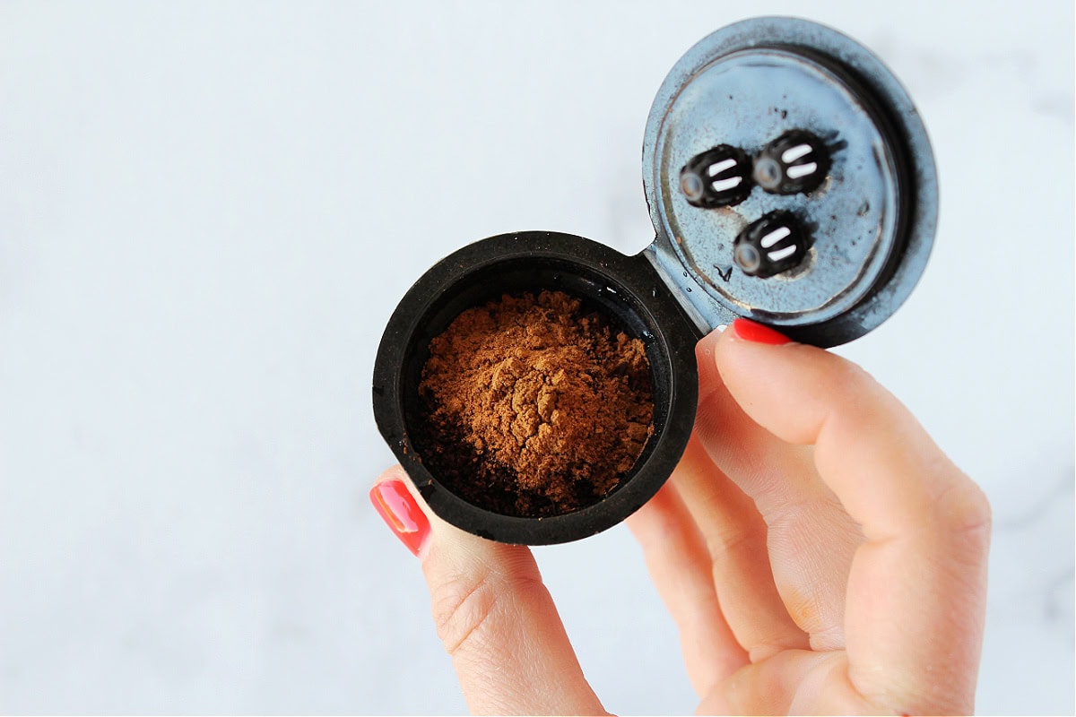 A woman's hand holding a reusable K-cup with coffee grounds and pumpkin pie spice.