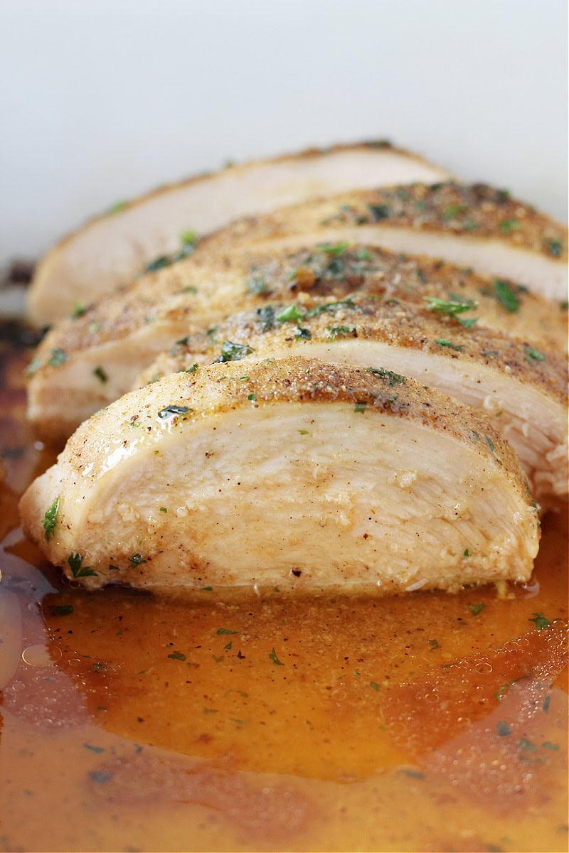 Sliced juicy baked chicken breasts in melted butter in the pan.