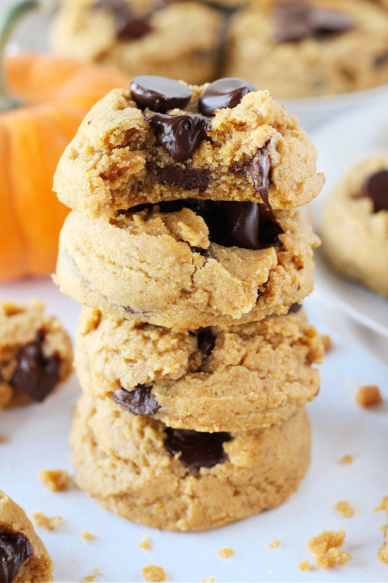 A stack of four pumpkin chocolate chip cookies with a bite taken out of one.
