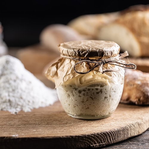 Sourdough starter in a glass jar with brown paper and twine on top.