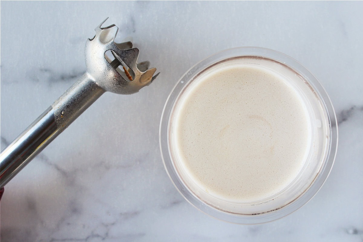 A stick blender beside a pint of milk, protein powder and pumpkin pie spice blended.