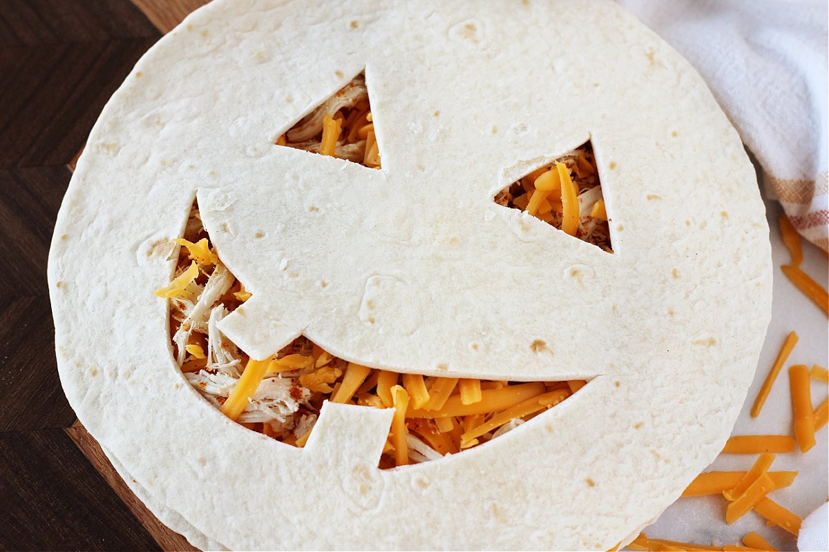 A Jack O' lantern face carved into a tortilla on a cheese and chicken quesadilla.