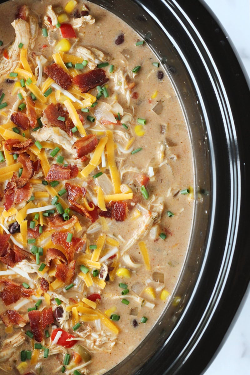 Crack chicken chili in a slow cooker topped with bacon and shredded cheese.