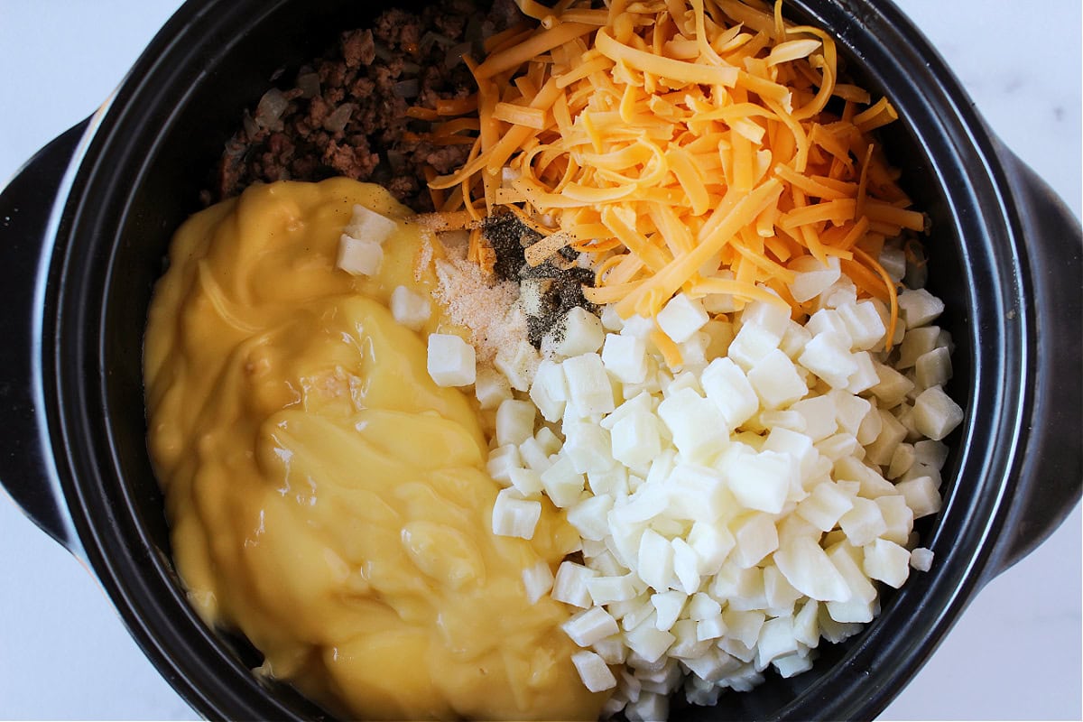 Shredded cheese, garlic salt, black pepper, cream of chicken soup, and potatoes in a pot.