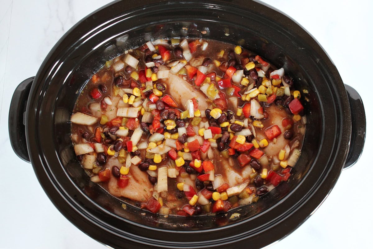 Raw chicken breasts mixed with black beans, veggies, and broth in a slow cooker.