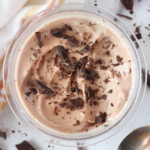 Chocolate chunks on ice cream in a Ninja Creami pint with a spoon on the side.