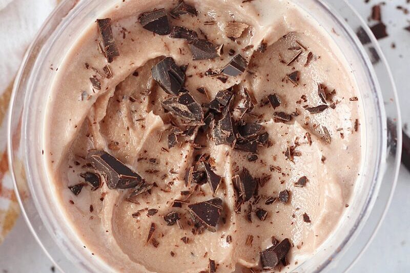 Chocolate chunks on ice cream in a Ninja Creami pint with a spoon on the side.