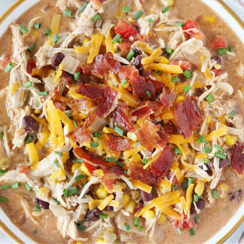 Bacon pieces, shredded cheese, and chives topping a bowl of crack chicken chili.