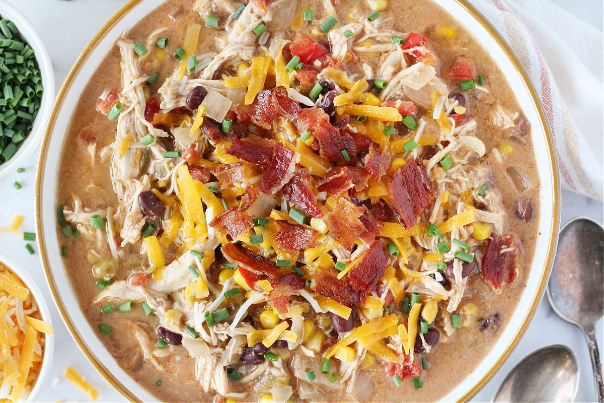 Bacon pieces, shredded cheese, and chives topping a bowl of crack chicken chili.