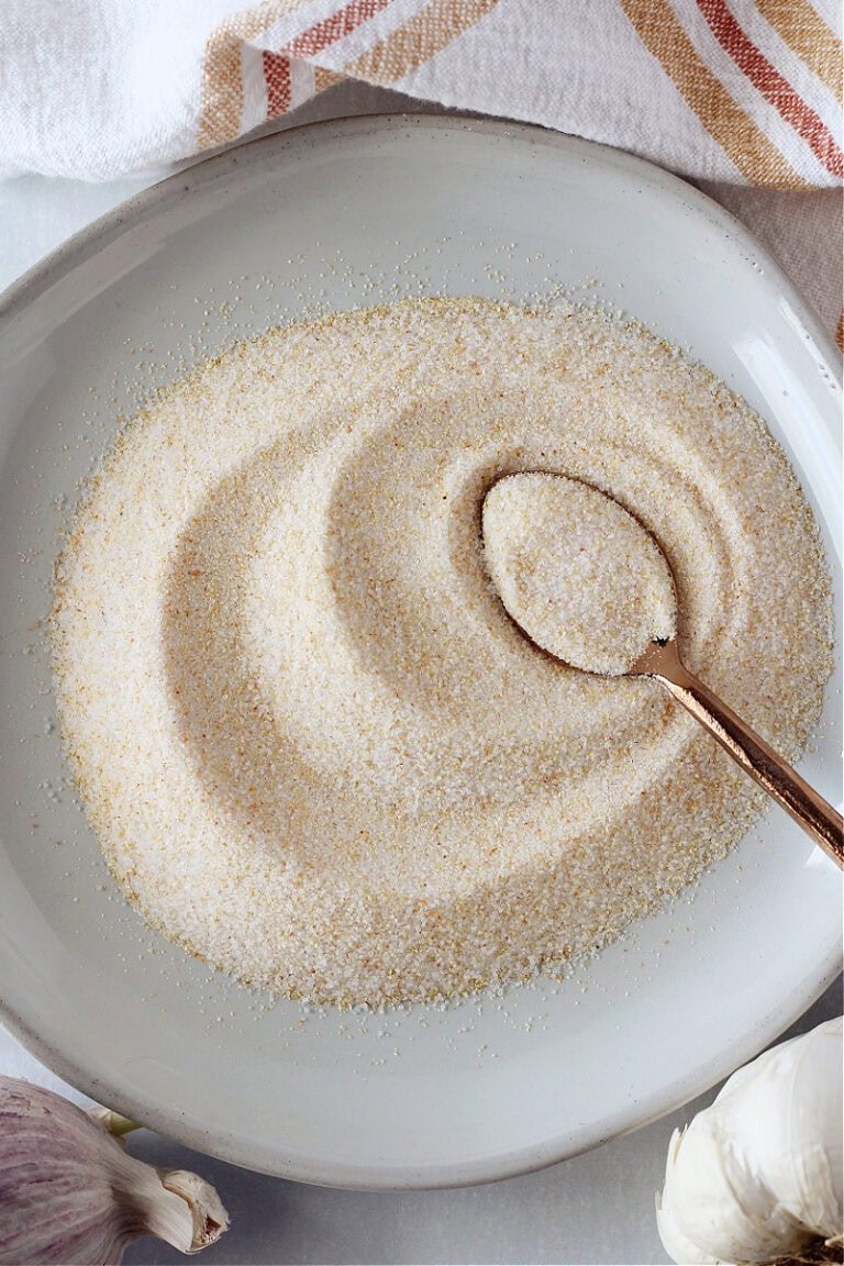 A copper spoon swirling garlic salt on a plate.