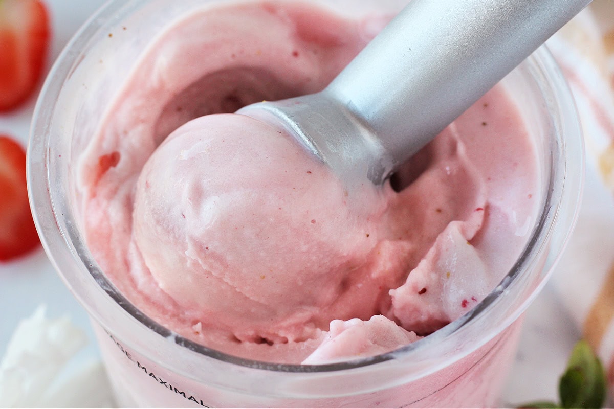Metal ice cream scoop in a Ninja Creami pint of strawberry ice cream.