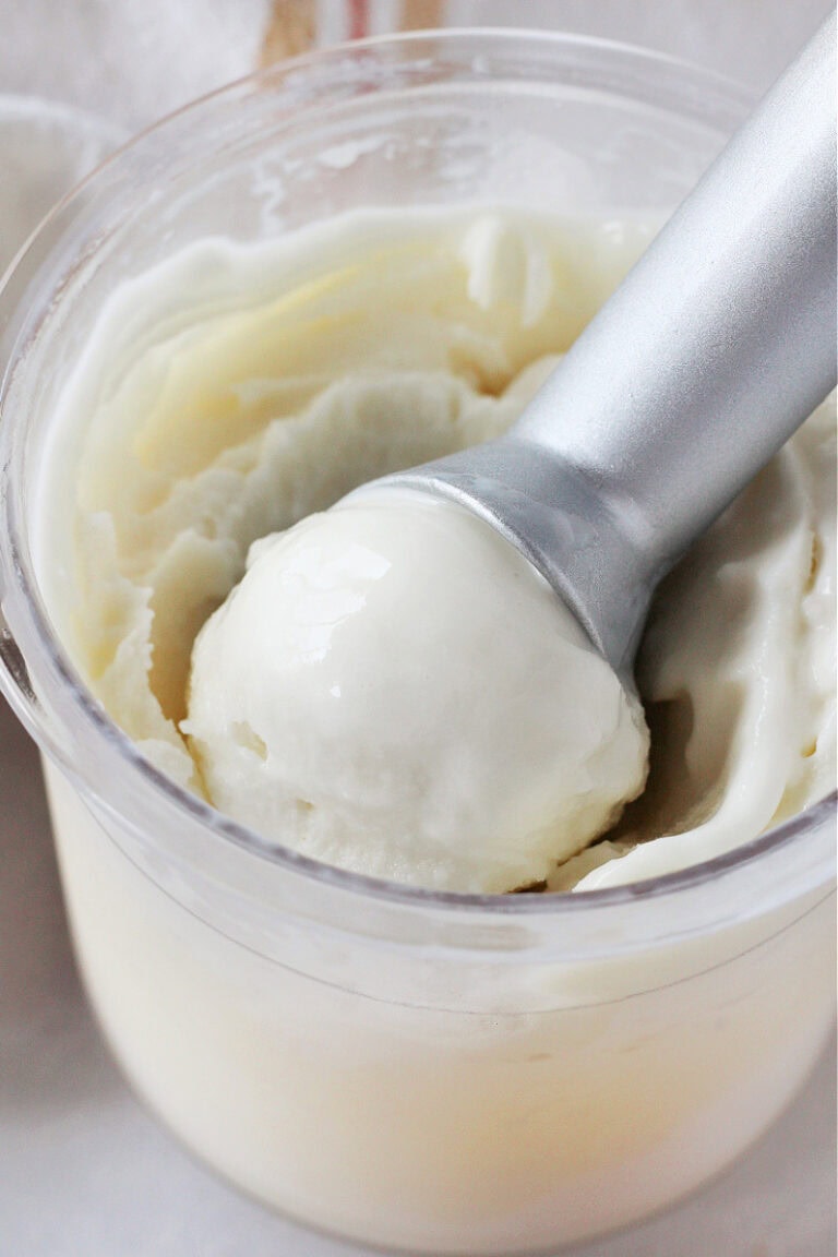 An ice cream scoop with vanilla ice cream in the Ninja Creami pint.
