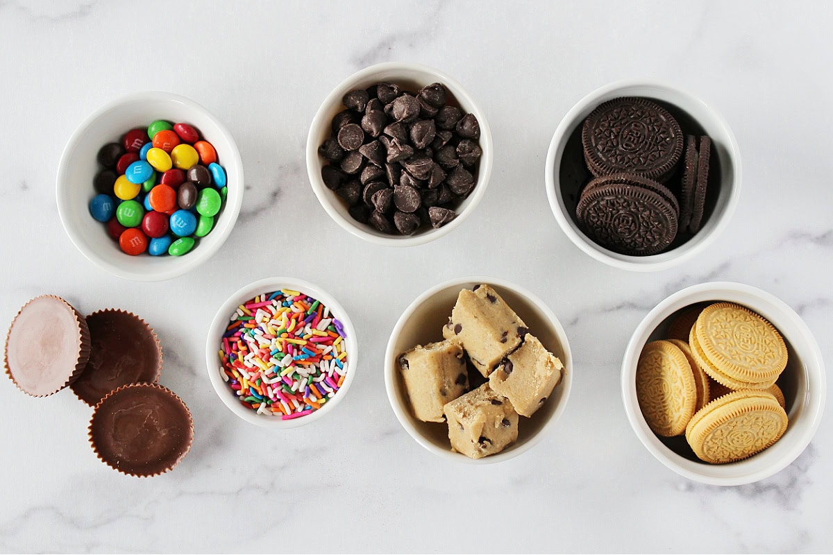 Candies, cookies, and sprinkles in cups on a white marble countertop.