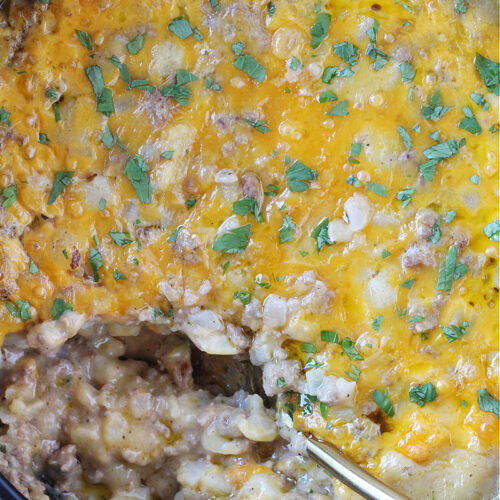 A large golden spoon in a cheesy ground beef and potato casserole.
