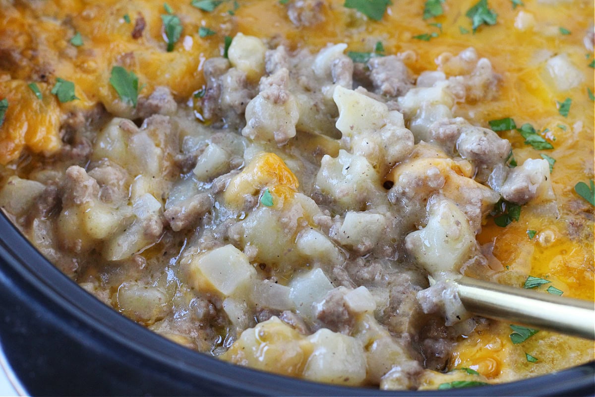 A spoon getting a scoop of cheesy ground beef and potato casserole.