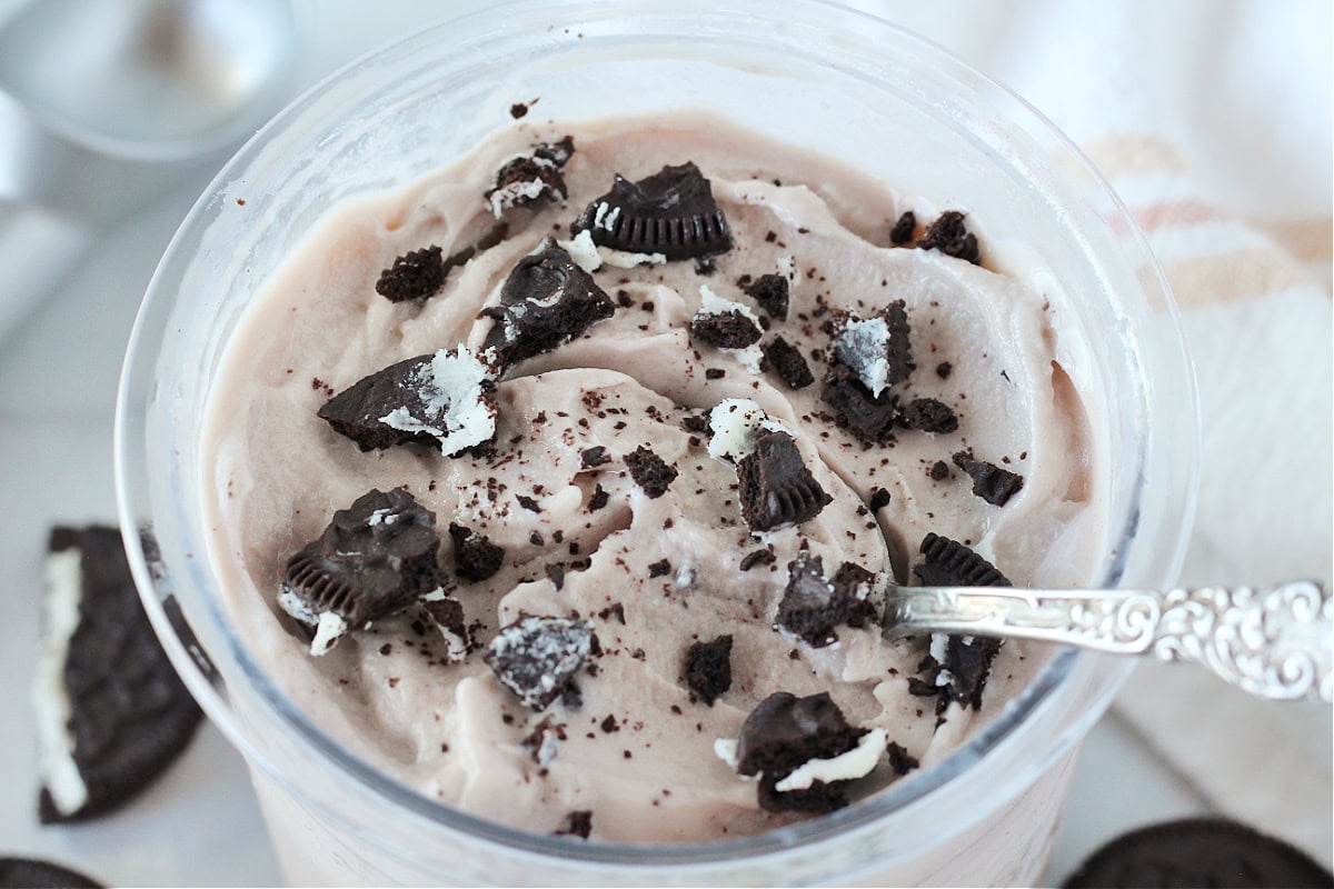 A spoon in a pint of Ninja cookies and cream ice cream topped with Oreos.