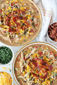 Crack chicken chili in two bowls topped with bacon, shredded cheese, and chives.