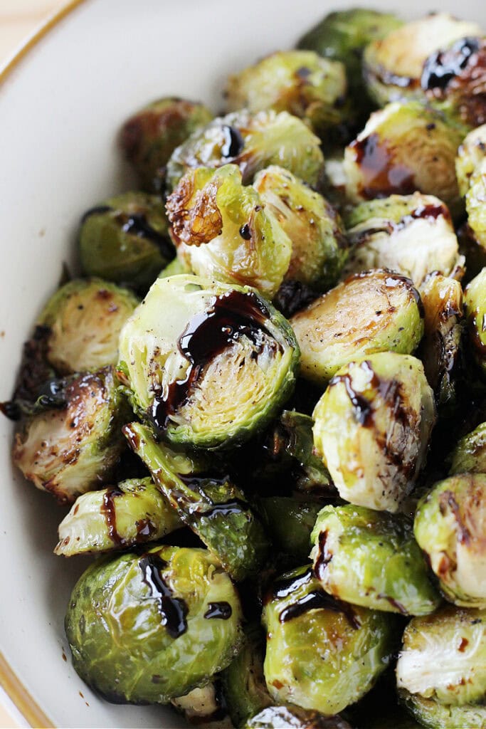 Roasted Brussel sprouts with balsamic glaze in a white serving bowl.