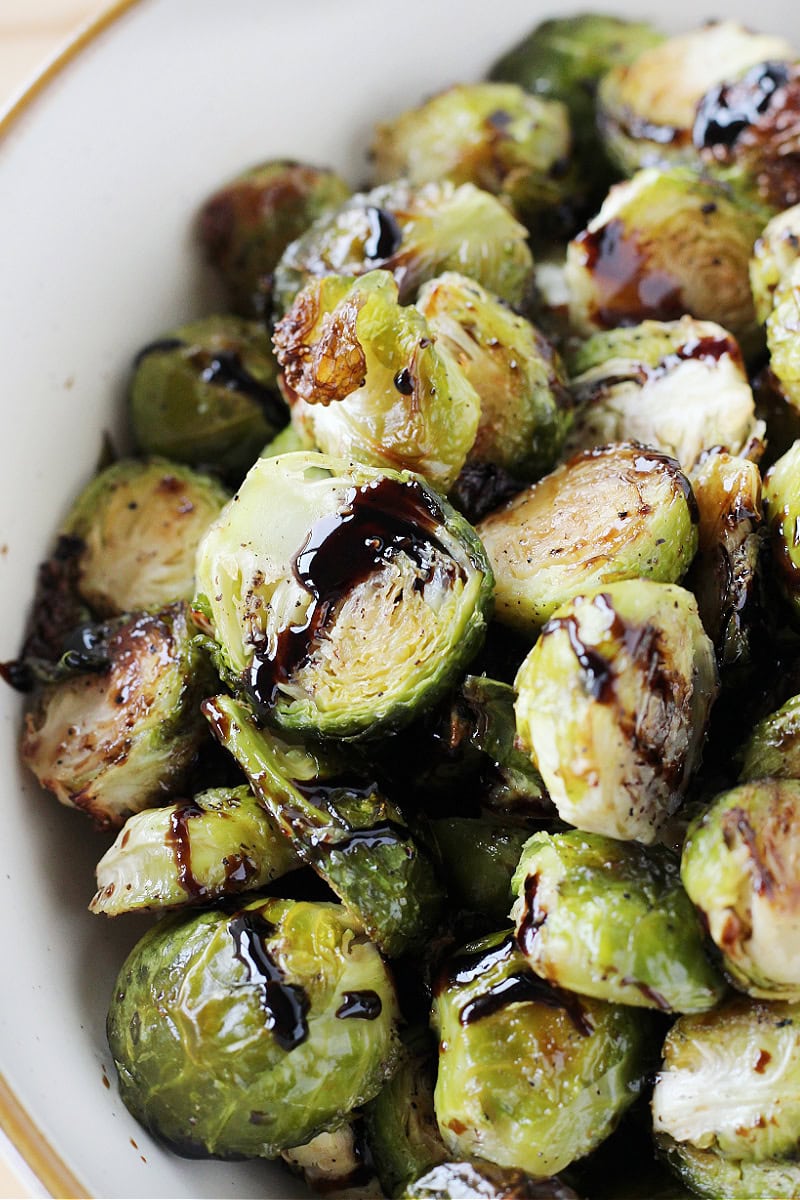 Roasted Brussel sprouts with balsamic glaze in a white serving bowl.