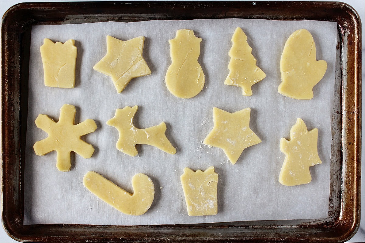 Unbaked cutout sugar cookie in Christmas shapes on a parchment lined baking sheet.