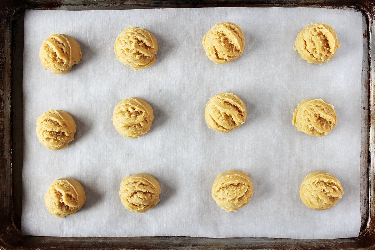 Twelve cookie dough balls on a parchment lined baking sheet.