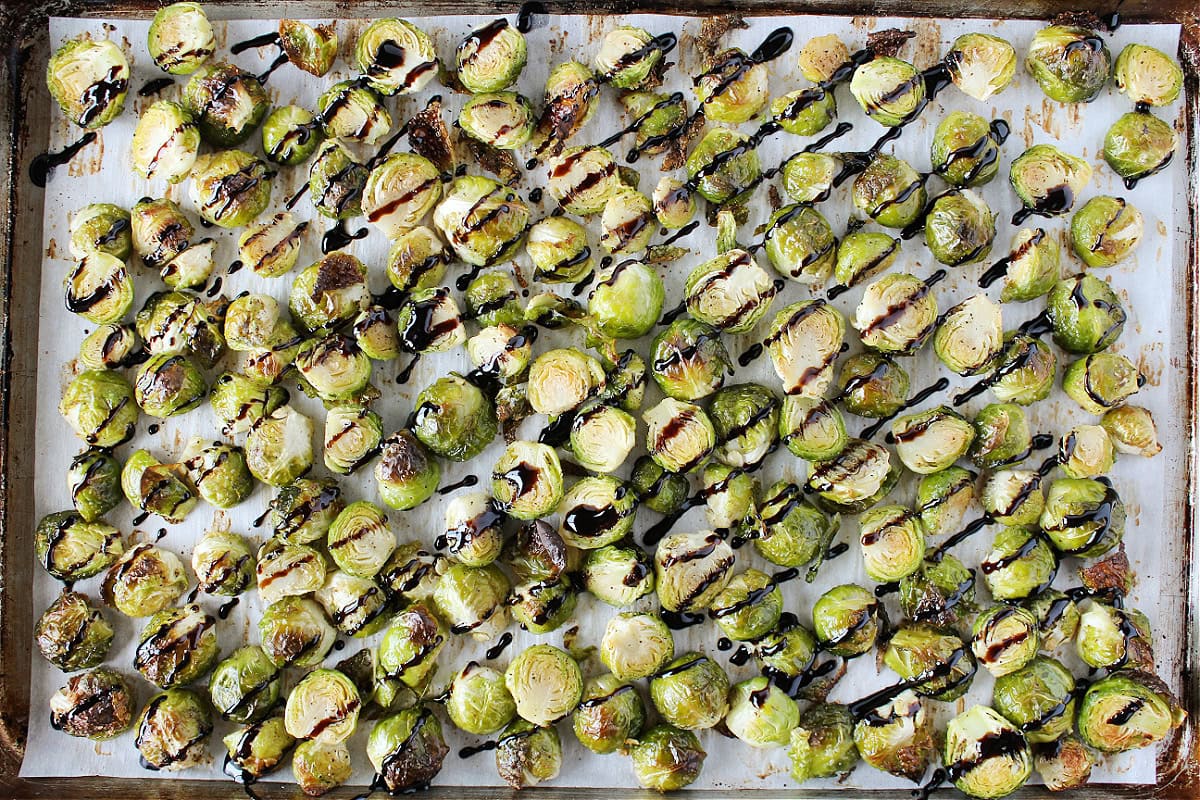 Roasted balsamic Brussel sprouts on a baking sheet drizzle with balsamic glaze.