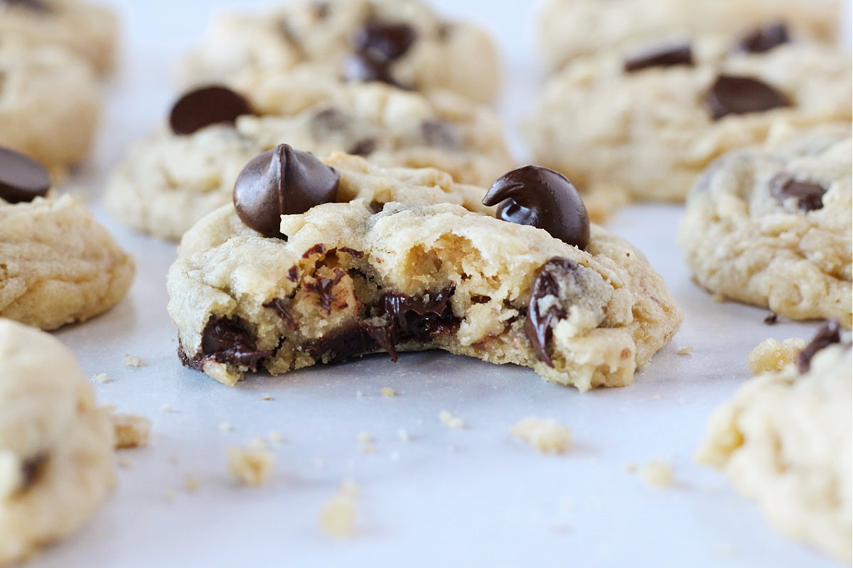 A bite taken out of a warm oatmeal chocolate chip cookie on a grey countertop.