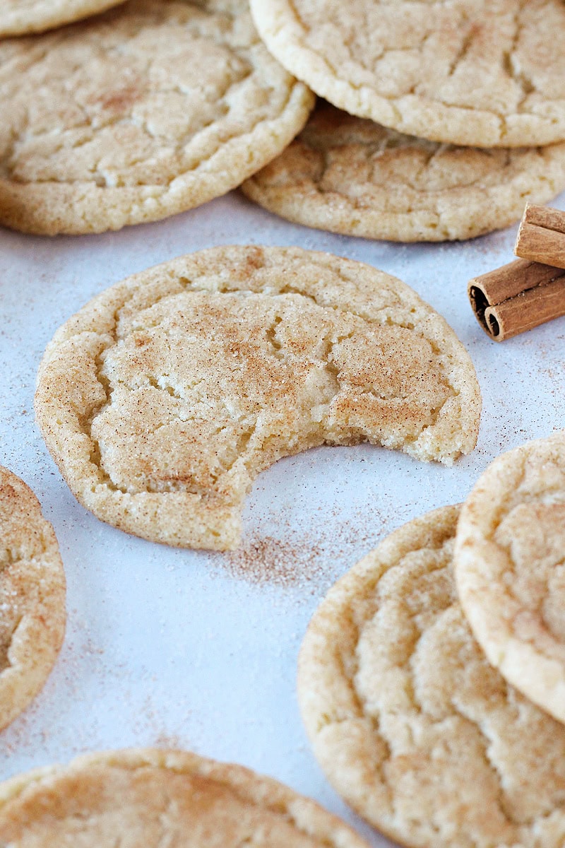 A bite taken out of a snickerdoodle cookie surrounded by cookies and cinnamon sticks.
