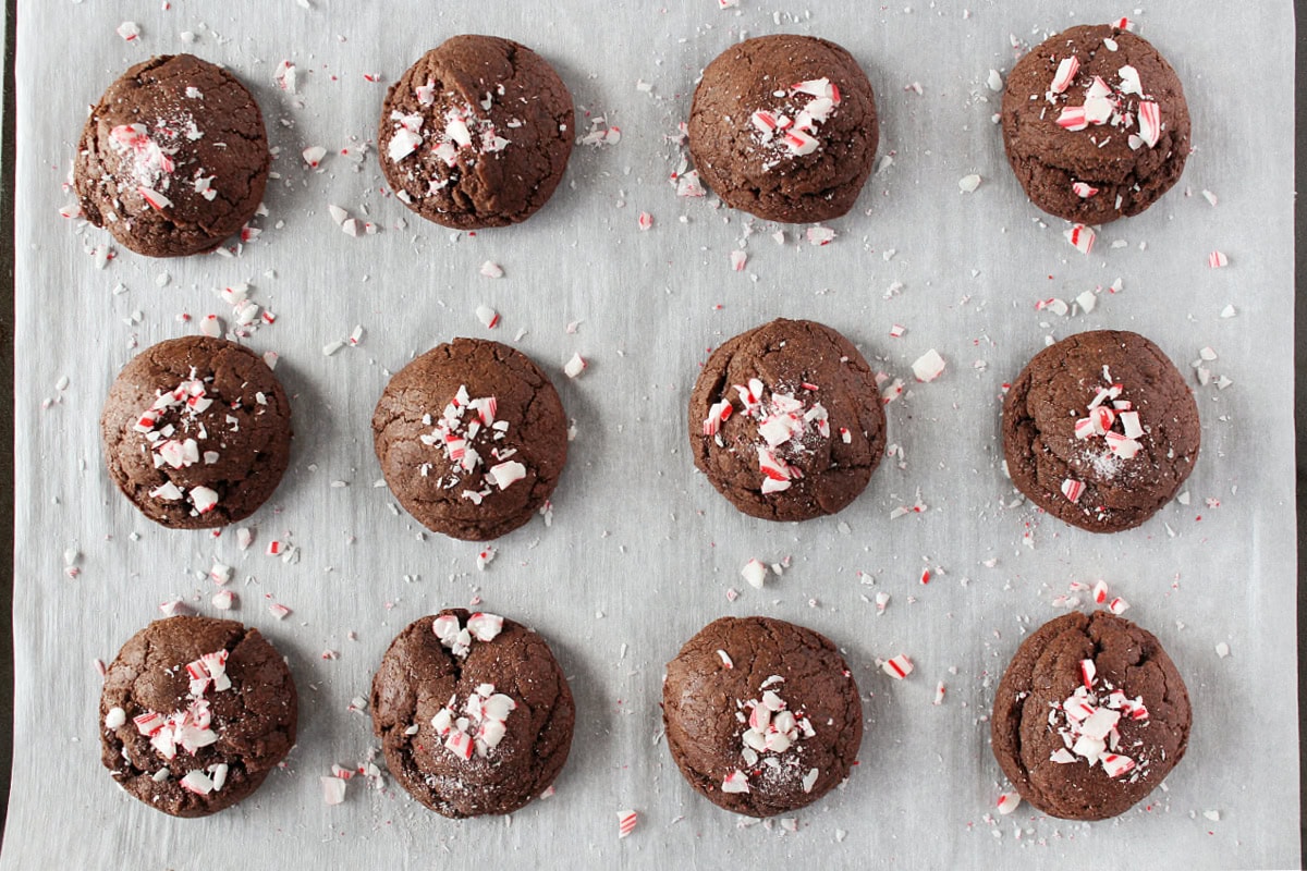 Twelve brownie cookies topped with crushed candy canes on a parchment paper lined baking sheet.