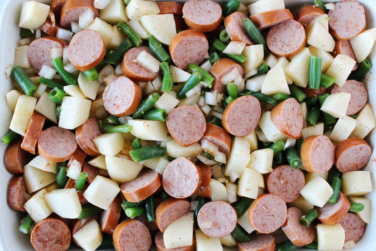 Seasonings on turkey sausage, potatoes and green beans in a white baking dish.