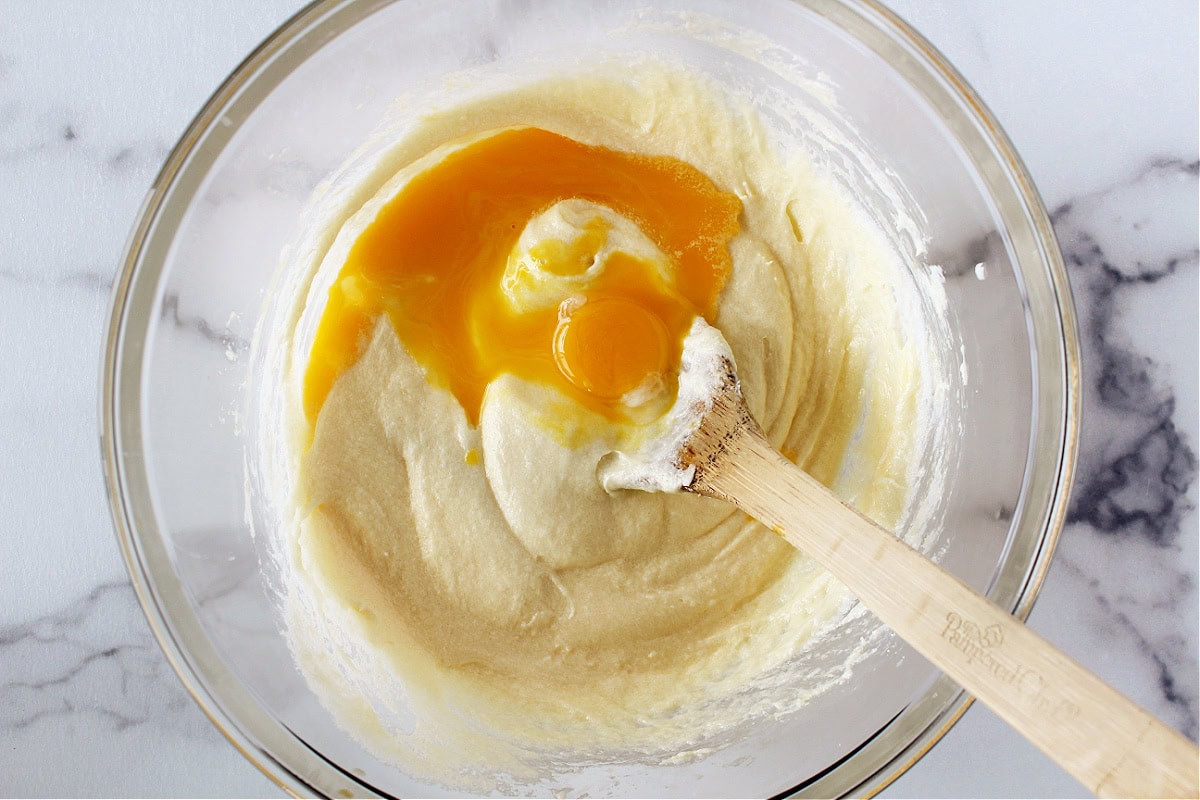 Egg yolks and a wooden spoon in creamed butter and sugar.
