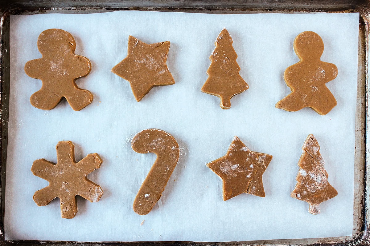 Eight unbaked gingerbread cutout cookies on a parchment lined baking sheet.