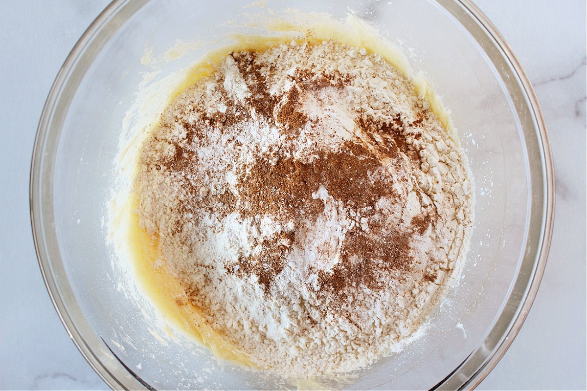 Cinnamon and flour on wet batter in a glass mixing bowl.
