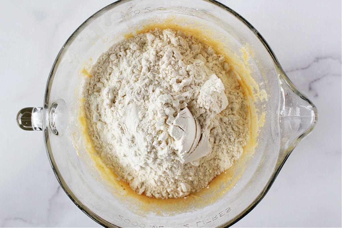 Flour on top of wet batter for cookies in a glass mixing bowl.