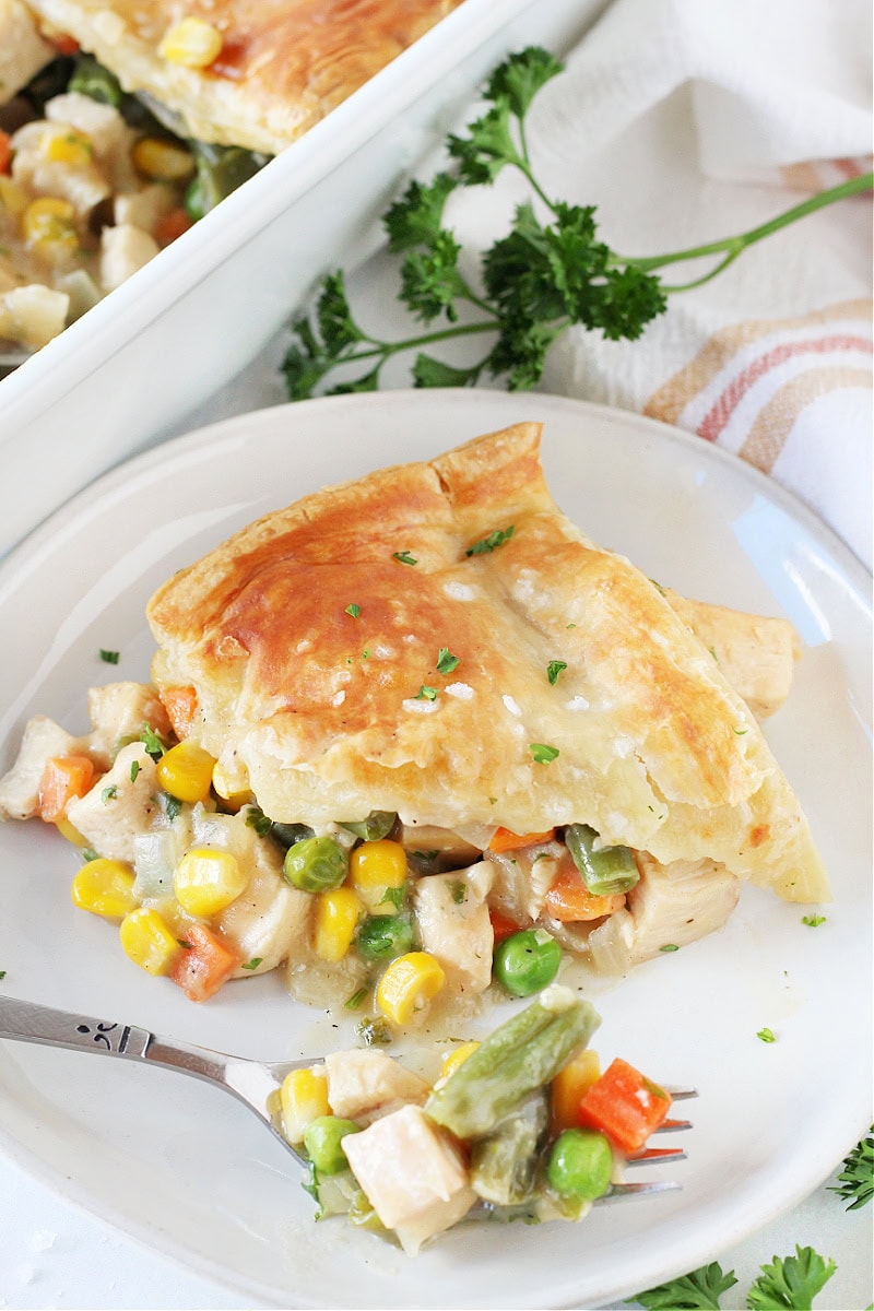A slice of homemade chicken pot pie on a white plate with a fork.