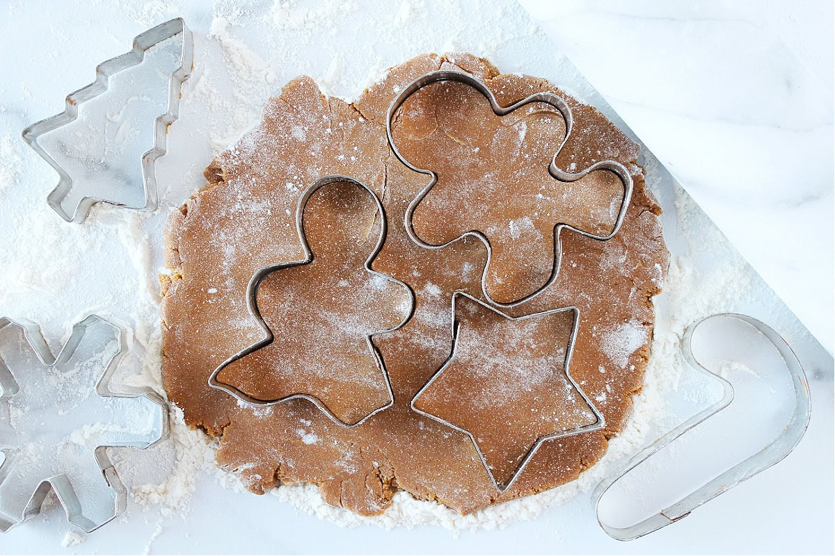 Three holiday cookie cutters pressed into gingerbread cookie dough.