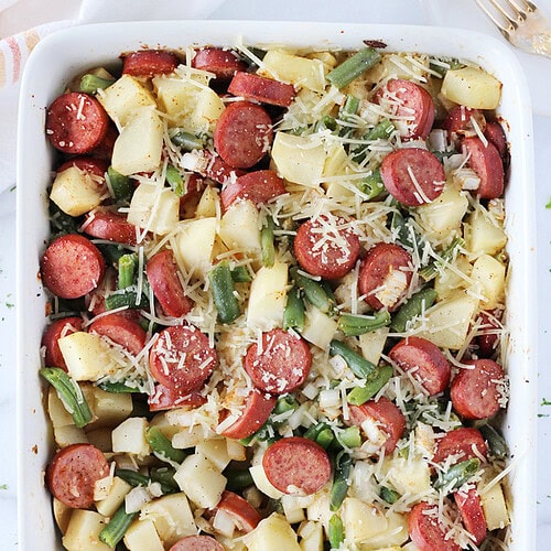 Diced potatoes, sliced sausage, and greens beans baked in a white 9x13 pan.